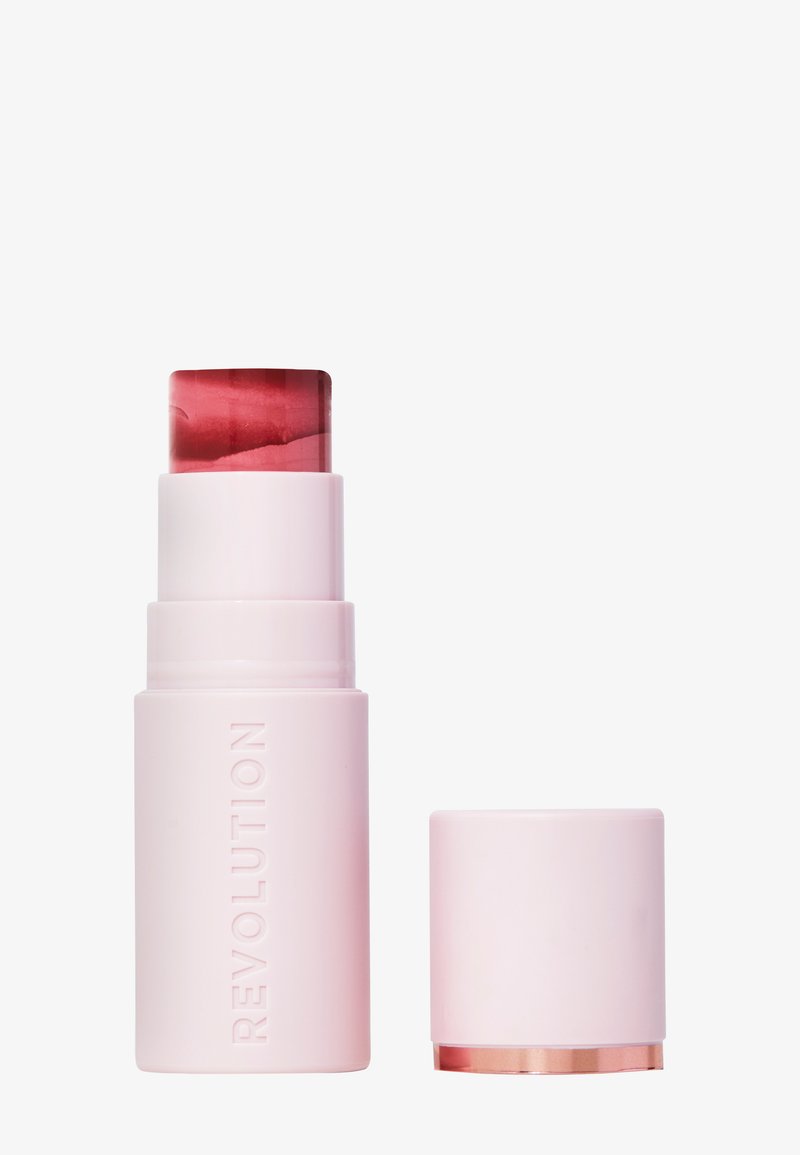 Stick de rubor en crema de Revolution en un contenedor cilíndrico rosa con una tapa roja transparente. Presenta una tapa extraíble con un acento dorado.
