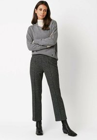 Szary sweter z dzianiny z dekoltem w serek, zestawiony z czarno-białymi spodniami w jodełkę. Modelka nosi czarne botki za kostkę.