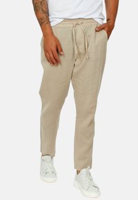 Pantaloni di lino beige con vita regolabile, dotati di tasche laterali e una vestibilità affusolata. Abbinati a sneakers bianche.