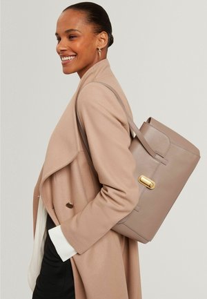 Borsa tote in pelle grigia con design strutturato, dettagli in oro e doppie cinghie per spalla, indossata da una modella con cappotto beige.