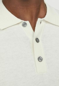 Kort�ærmet polo skjorte i off-white, strikstof med en blød tekstur. Har en klassisk krave og tre metallisk grå knapper.