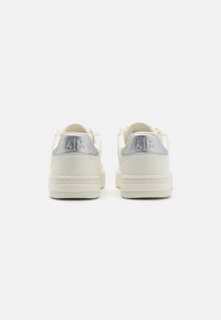 White leather sneakers feature a smooth texture, round toe, and a subtle silver accent on the heel with embossed logo detail.
