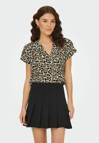 Leopardmönstrad t-shirt med kort ärm och V-ringning, i kombination med en svart plisserad kjol, tillverkad av lättviktsmaterial.