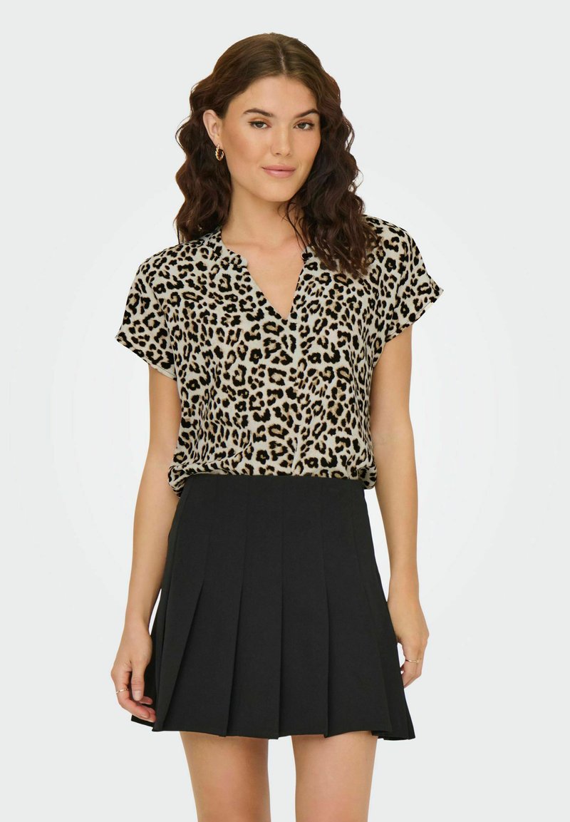 Leopardmönstrad t-shirt med kort ärm och V-ringning, i kombination med en svart plisserad kjol, tillverkad av lättviktsmaterial.