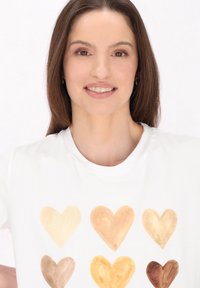 Hvid t-shirt med seks hjerte-designs i forskellige hudfarver. Korte ærmer og rund halsudskæring, lavet af glat bomuldsstof.