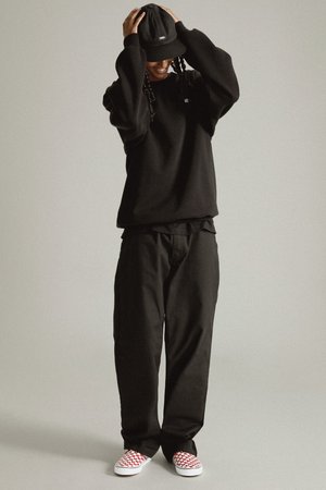 Black sweat top with oversized fit, paired with matching loose black trousers. Features red-and-white checkered slip-on shoes and a black cap.