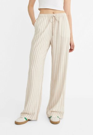 Beige og hvide lodrette stribede bukser med vidde ben og snøre i taljen, båret med hvide sneakers med grønne detaljer og en hvid cropped top.
