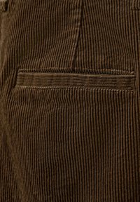 Gros plan d’un tissu en velours côtelé marron avec une poche passepoilée horizontale cousue dans le matériau texturé.