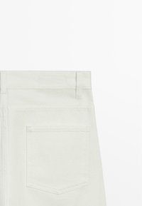 Weißes Denimstück, das den hinteren Bund mit Gürtelschlaufen und eine auf der rechten Seite angenähte einzelne Gesäßtasche zeigt.