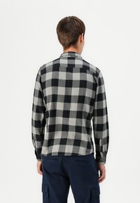 Camisa de franela a cuadros en negro y gris, de manga larga, con puños abotonados, detalle de pliegue en la espalda, textura suave, corte casual.