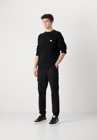 Zwarte gebreide trui met ribbelstructuur, zwarte cargo pants met zijzakken en zwarte sneakers met witte accenten en logo-details.
