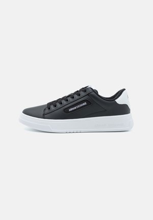Svart syntetisk sneakersko med vit gummisula. Har varumärkeslogotyp på sidan, rund tå och snörning fram. Ren, minimalistisk design.