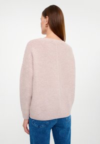 Light pink striped sweater with a relaxed fit, featuring ribbed cuffs and hem, and a smooth texture. Worn over blue denim jeans.