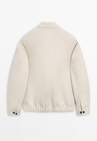 Beige langärmelige Jacke mit elastischem Saum, geknöpften Manschetten und einem kleinen Kragen, von hinten auf weißem Hintergrund gezeigt.