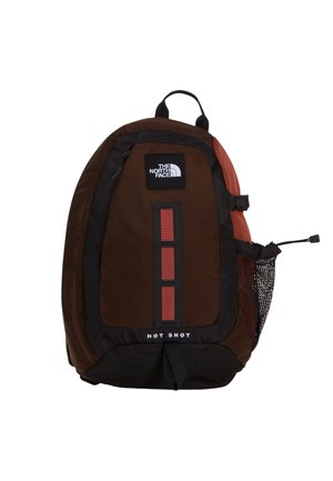 Brauner und schwarzer The North Face Hot Shot Rucksack mit roten Akzenten, vorderen vertikalen Schlaufen und seitlichem Netz-Wasserflaschenhalter.