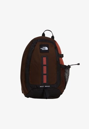 Brązowy i czarny plecak The North Face Hot Shot z czerwonymi akcentami, pionowymi pętlami z przodu oraz boczną siateczkową kieszenią na butelkę wody.