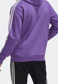 Lila huvtröja med en mjuk textur, prydd med vita randdetaljer längs axlarna och matchande svarta sweatpants.