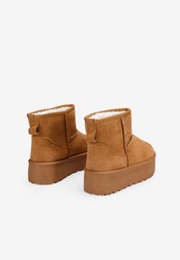 Botas de ante marrón hasta el tobillo con un interior suave, una suela de plataforma gruesa y detalles en bucle en la parte posterior para facilitar su uso.