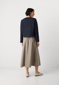 Sudadera recortada de color navy con mangas largas, combinada con una falda midi beige. El atuendo se completa con zapatos de tonalidades claras.