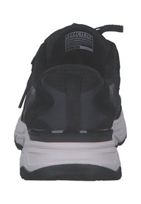 Svart och vit atletisk sneaker sedd bakifrån, med en dragflik, texturerad sula och storleksmärke inuti hälområdet.