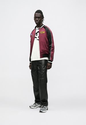 Tēja sarkans satīna bomber jaka ar plāksteriem, balts grafiskais džemperis, melnas ādas cargo bikses un melni balti apavi.