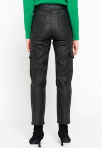 Svarta byxor i konstläder med cargo-design, med en åtsittande midja, två sidofickor och en slät ytstruktur, matchade med svarta ankelboots med klack.