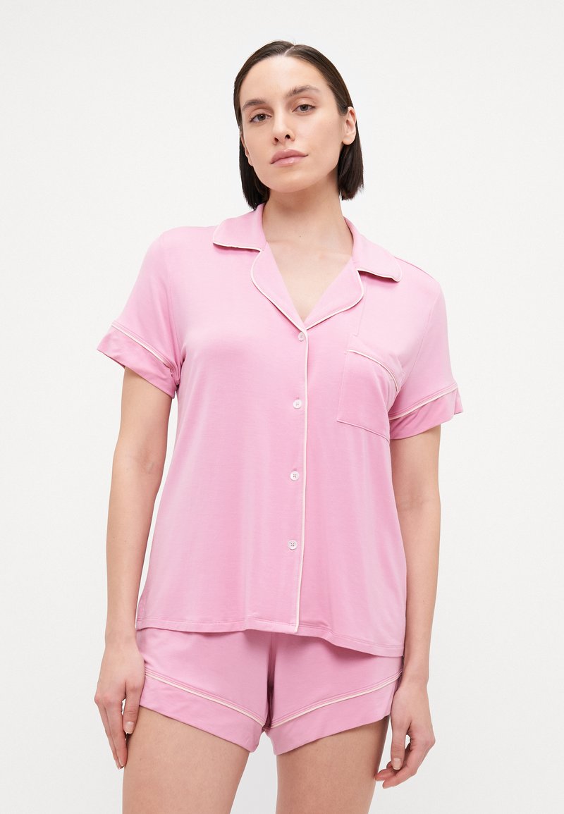 Conjunto de pijama rosa em tecido suave, apresentando uma blusa de manga curta com colarinho e um bolso, e calções coordenados com detalhes em viés.