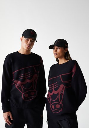 Maglioni neri a maglia con una grande grafica di un toro bordeaux sulla parte anteriore, abbinati a cappellini neri con un logo simile del toro.
