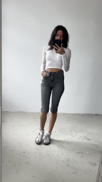 Fehér, hosszú ujjú cropped top, szürke, térdig érő farmernadrág és szürke sportcipő fekete részletekkel. Tükörfényes háttér.