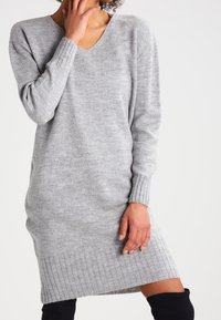 Robe-pull gris en maille avec un décolleté en V, des poignets et un ourlet côtelés. Présente une coupe décontractée et une texture douce, s'étendant jusqu'à mi-cuisse.