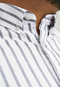 White shirt with navy-blue stripes, button-down collar, and two buttons on the collar. Fabric appears soft with a smooth texture.