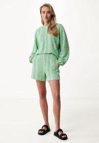 Zelený texturovaný loungewear set s dlouhým rukávem a odpovídajícími kraťasy, doplněný černými sandály na pásky.