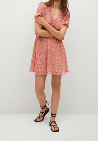 Robe florale rose avec des manches courtes bouffantes, décolleté en v et coupe décontractée. Associée à des sandales noires à lanières. Tissu doux et léger.