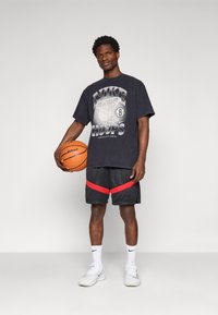 Černé grafické tričko s nápisem "NIKE HOOPS", šedý design basketbalu. Černé šortky s červenými pruhy. Bílé tenisky a basketbal.