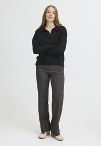 Juodas megztinis su apykakle, derinamas su pilkomis kelnėmis. Modelis vilki smėlio spalvos sportbačius su tamsiomis juostelėmis. Paprastas, švarus dizainas.