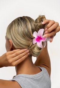 Plastisk hårklämma i form av en blomma med rosa och vita kronblad. Slät yta, håller en tvinnad knut frisyr på plats.