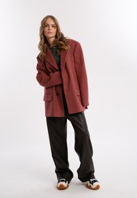 Przesadny bordowy blezer o fakturowanej tkaninie, z dwiema przednimi kieszeniami, zestawiony z szerokimi czarnymi spodniami i wielokolorowymi trampkami.