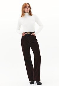 Witte coltrui, donkerbruine corduroy brede broek met zijzakken, en een grote, ovale gesp riem gecombineerd met zwarte hakken.