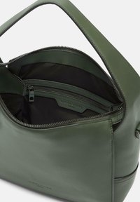 Zielona skórzana torebka o strukturalnym kształcie, z zamykaną kieszenią i pojedynczym paskiem na ramię. Wnętrze wyłożone czarnym materiałem.