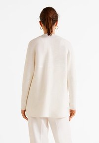 Pull en maille blanche à col montant à l'arrière et manches longues. Présente une coupe droite et une surface texturée. Design minimaliste.