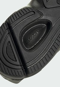 Čierna gumová podrážka športovej obuvi s textúrovaným povrchom, výraznými vzormi a polstrovanou časťou označenou "CLOUDFOAM."