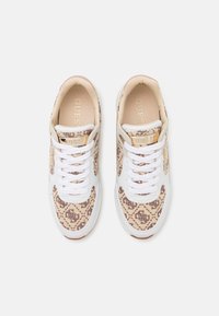Sneakers bianchi con tomaia in tessuto beige a fantasia e lacci bianchi. Presentano una soletta color sabbia con il logo "GUESS" e una suola in gomma marrone.