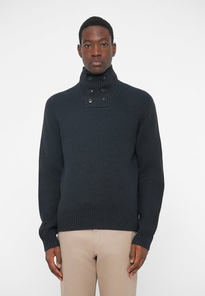 Pull en maille côtelée navy foncé avec un col montant, comportant deux boutons proéminents. Coupe boxy avec un motif texturé et un ourlet côtelé.