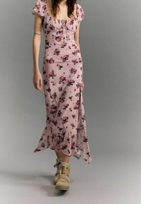 Blommig midiklänning i ljusrosa, med puffärmar, en rynkad halsringning och en volangkant. Matchas med ljusbruna platåskor.