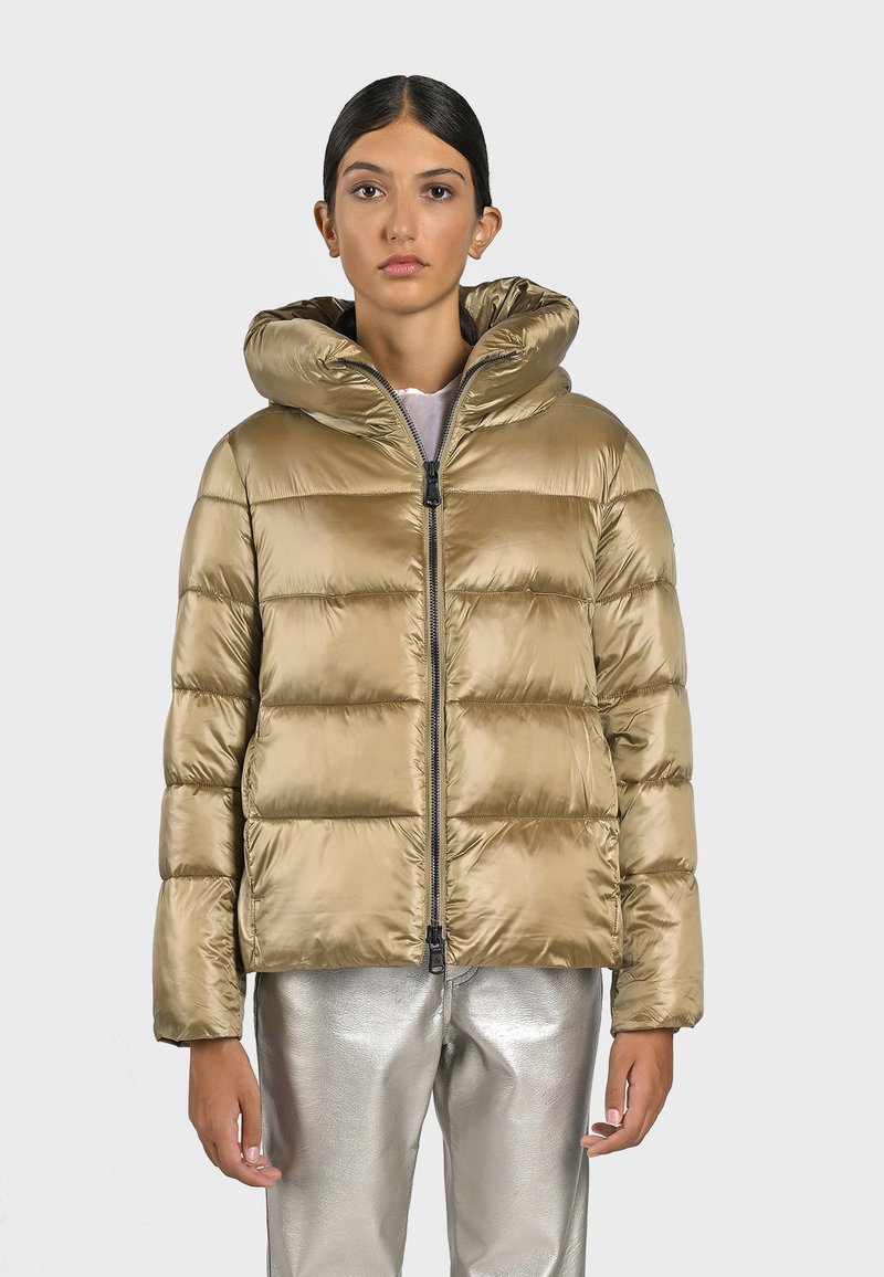 Giacca Puffer in oro metallico con cappuccio, dotata di sezioni trapuntate, una zip frontale e una finitura lucida. Abbinata a pantaloni argentati lucidi.