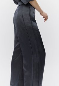 Παντελόνια με φαρδιά μπατζάκια σε σκούρο γκρι ύφασμα, με ομαλή υφή και εμφανείς πλαϊνές ραφές, άνετη εφαρμογή και ψηλή μέση.