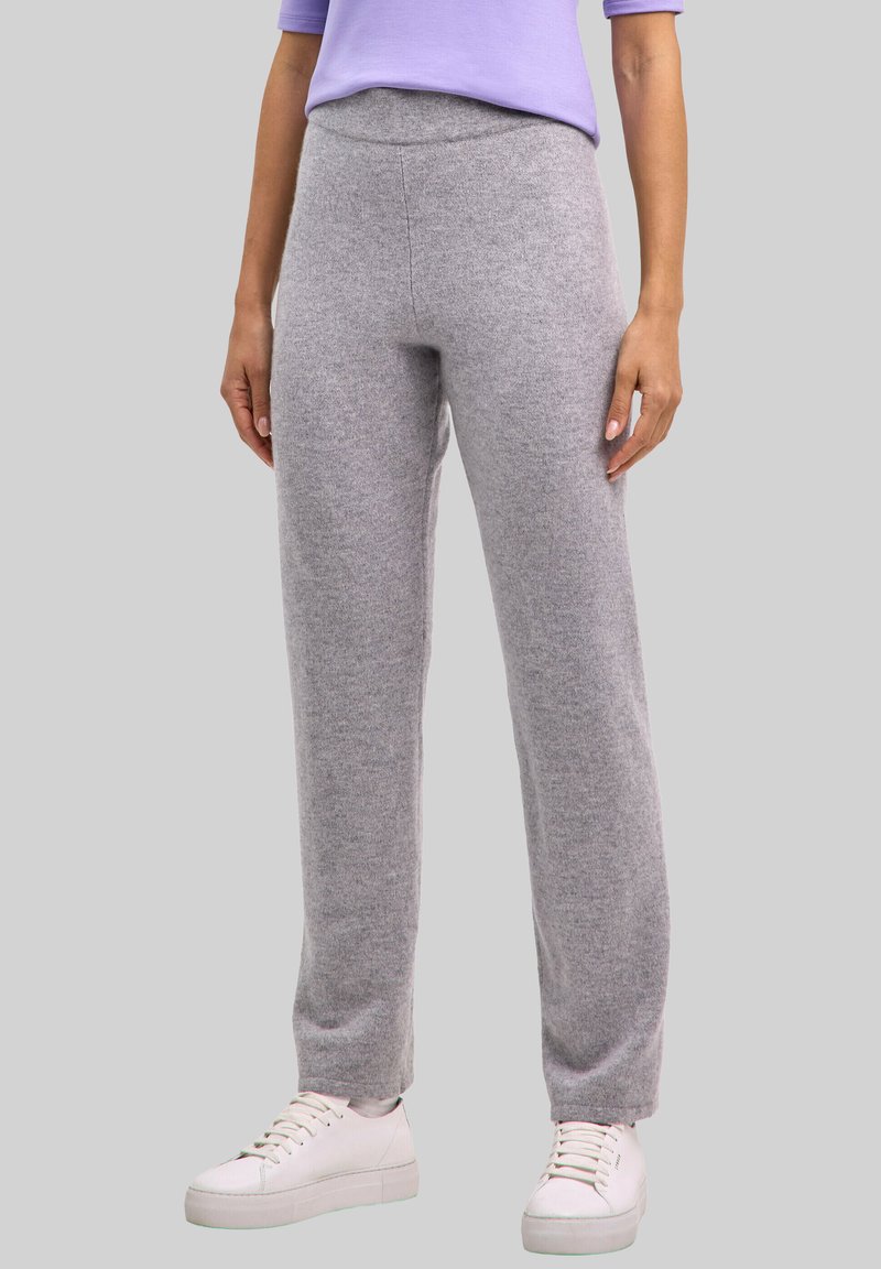 Grijze, zachte gebreide broek met een ontspannen pasvorm, voorzien van een naadloze tailleband en taps toelopende pijpen, gecombineerd met witte sneakers en een lavendelkleurige top.