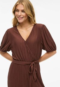 Ruda plisuota apykaklės su V formos iškirpte ir trumpomis pūstomis rankovėmis. Yra liemens juosta pritaikymui ir lygaus audinio tekstūra.