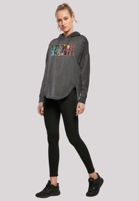 Felpa grigia con cappuccio e un audace grafica "MARVEL" multicolore. Abbinata a leggings neri e sneakers nere, con una vestibilità comoda.