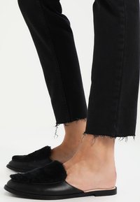 Svarta slip-on skor med en mjuk svart ovandel och slät beige sula, matchade med svarta jeans med fransar.